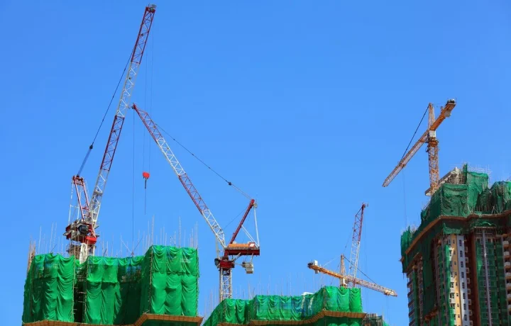 Construction management and inspection services - multiple cranes and building with safety netting.