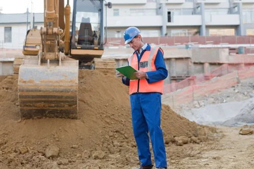 Residential construction management services - worker with clipboard in front of excavator.